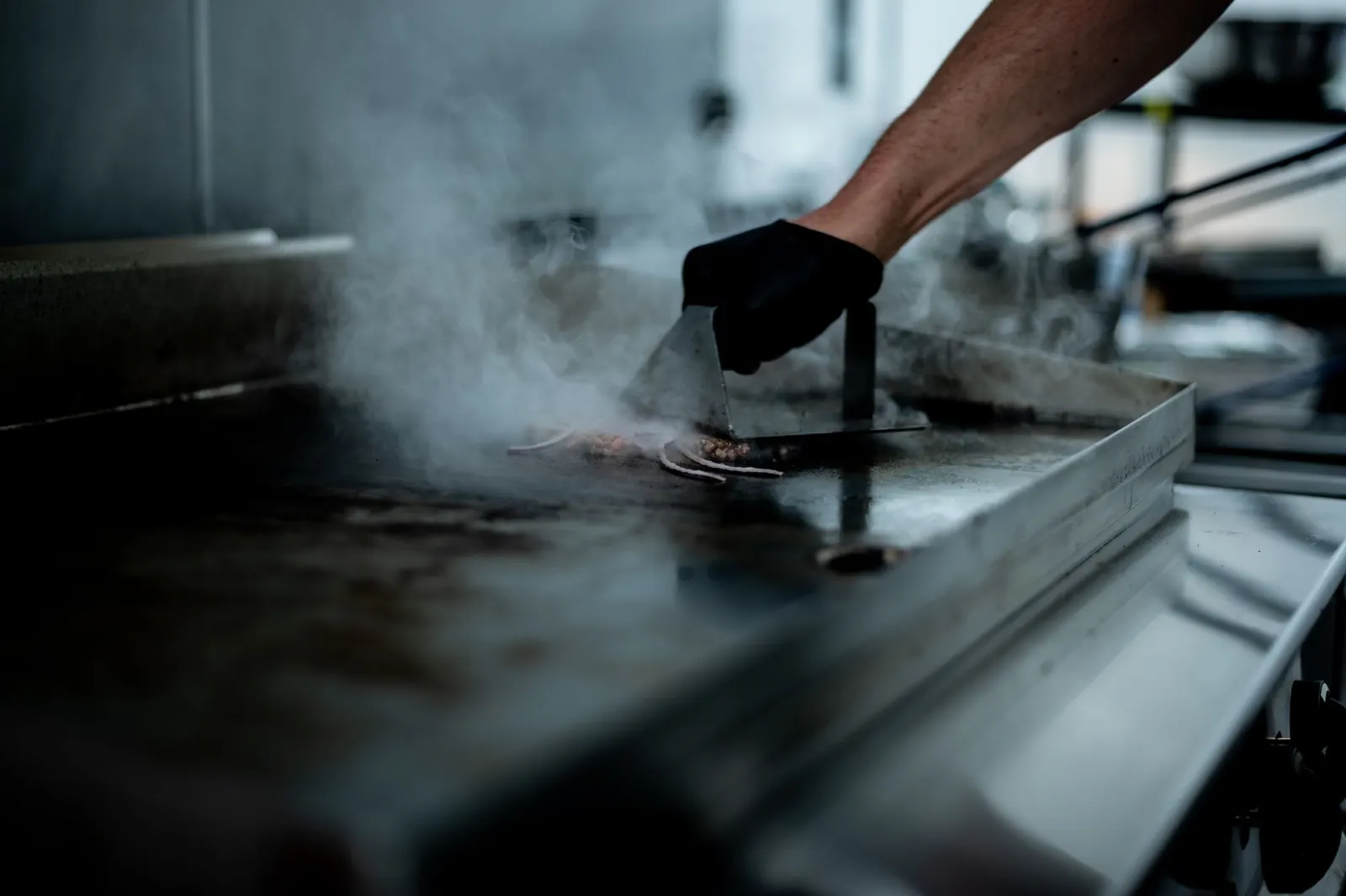 A cook working the flat-top griddle, steam rising